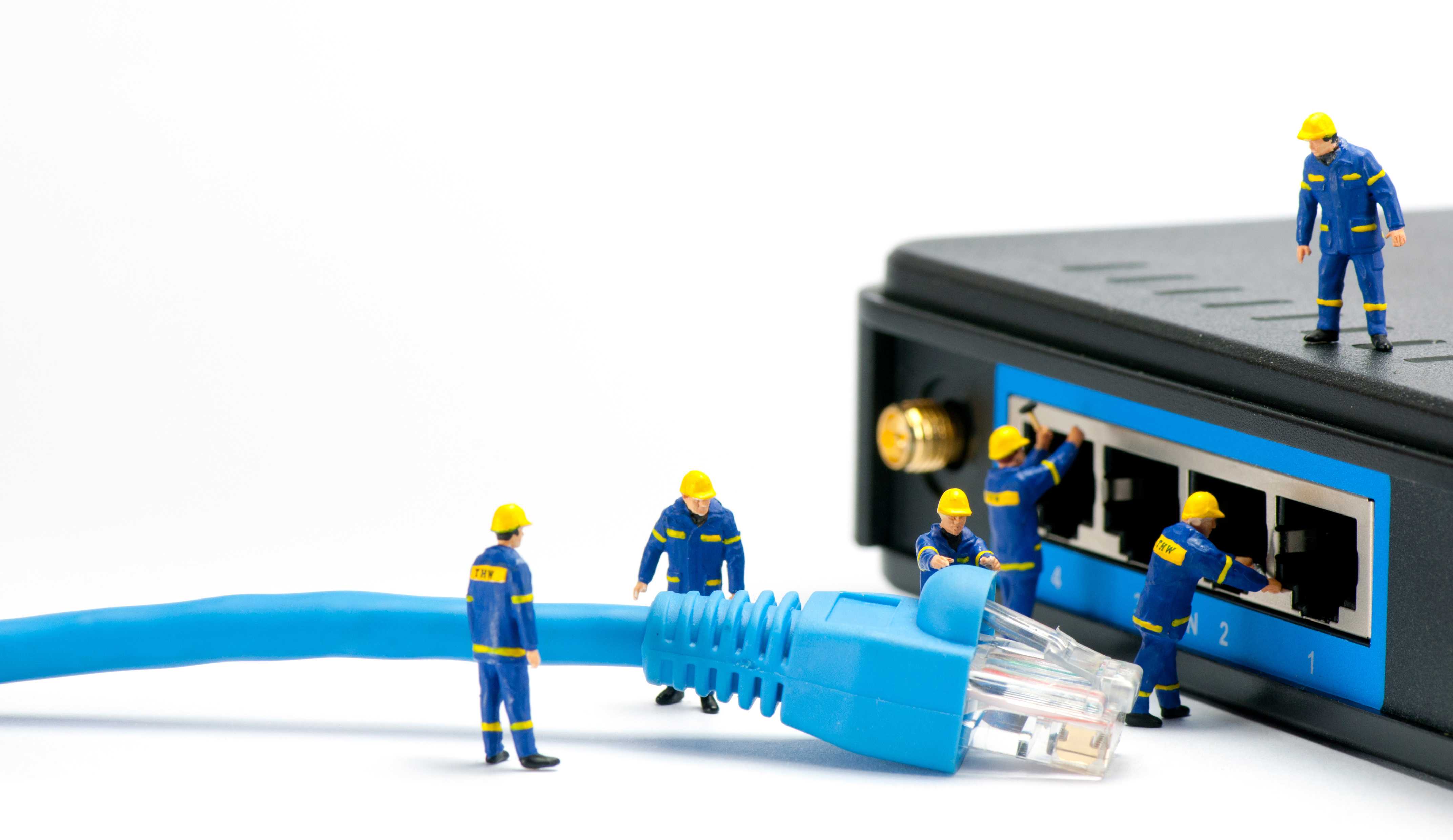 IT Solutions section - Team of miniature it technicians plugging in an Ethernet cable to into a switch.