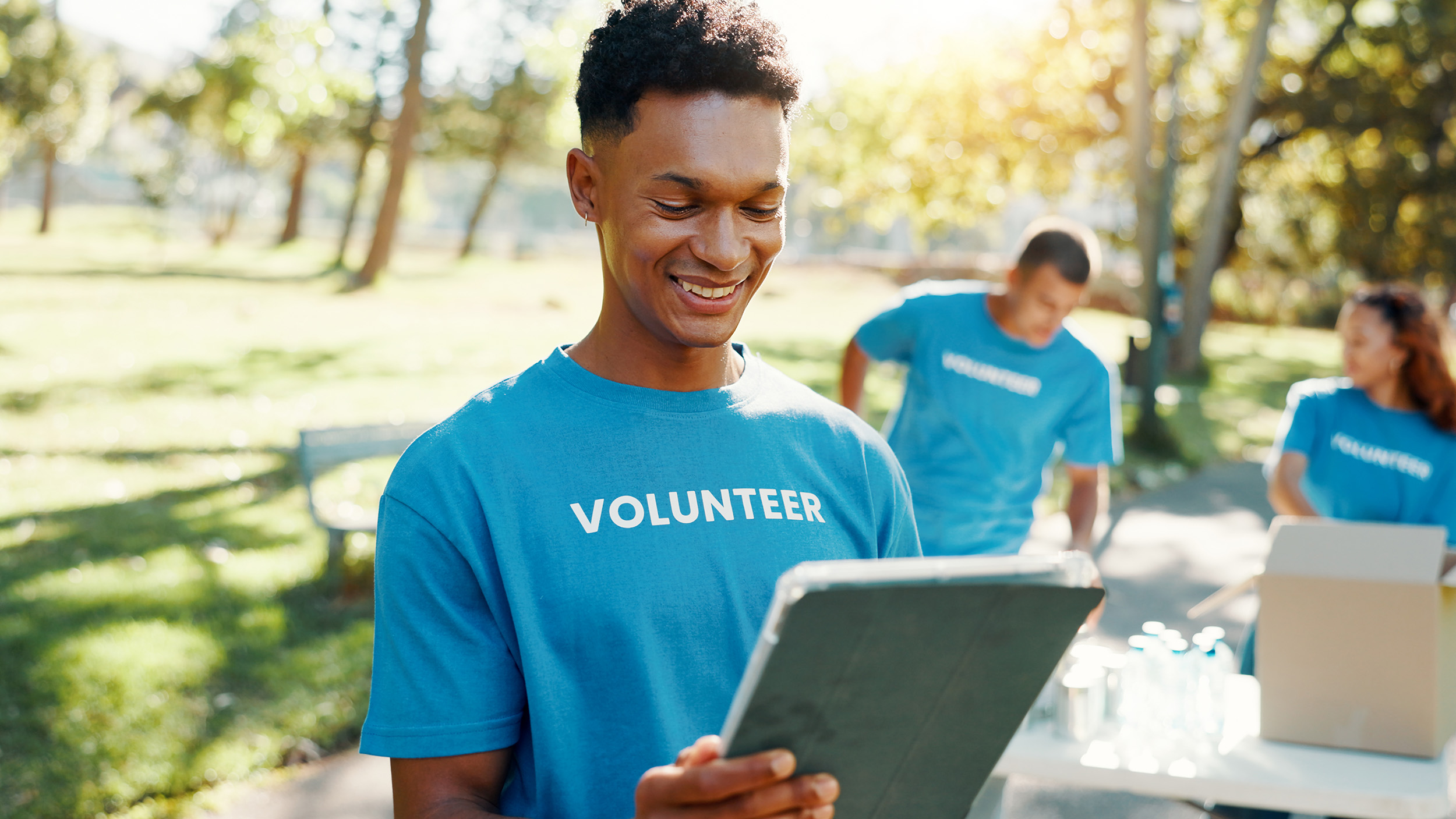 Volunteer using a tablet outdoors with team in background.